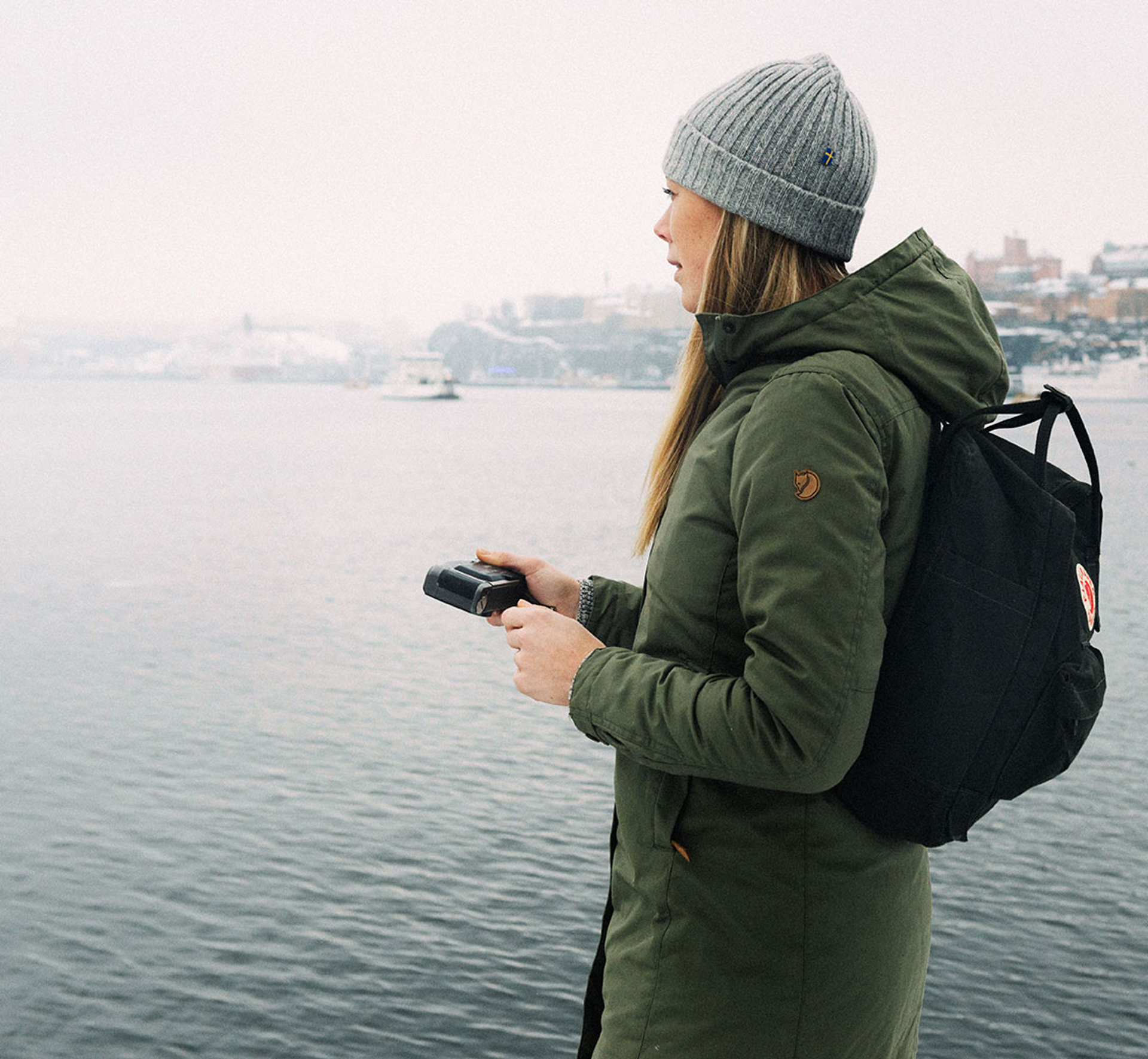 woman in fjallraven apparel standing by a river with a camera