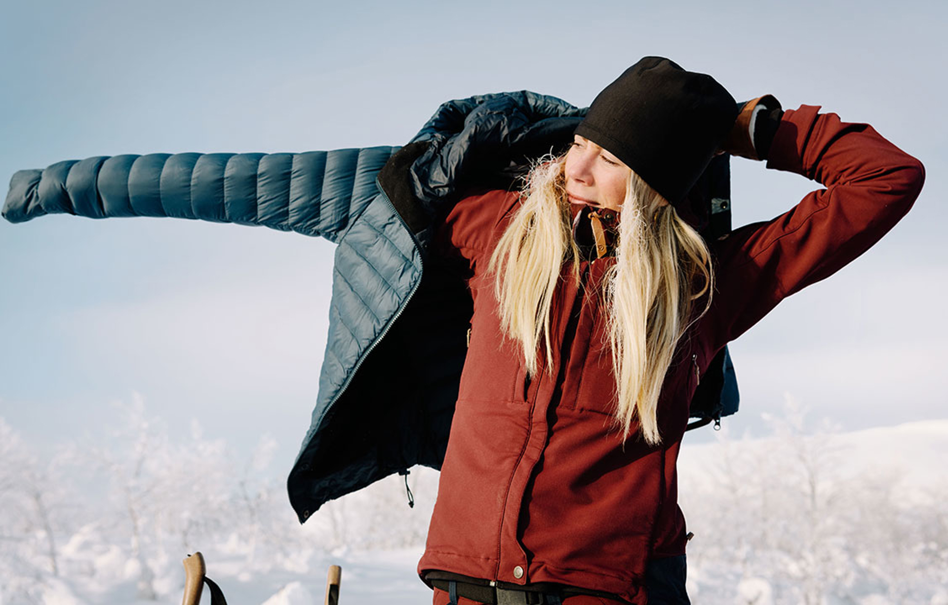 woman putting on a Fjallraven Keb Down coat over other Fjallraven apparel